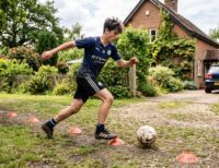 A young football player doing dribbling drills at home with cones in a garden, part of a home football training plan
