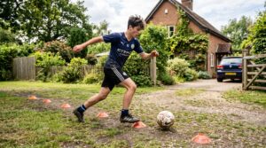 A young football player doing dribbling drills at home with cones in a garden, part of a home football training plan