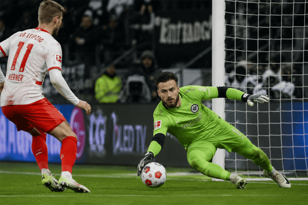 Diant Ramaj diving low to stop a close-range shot during a Bundesliga football match.