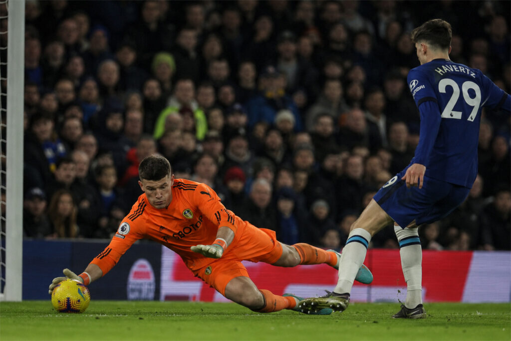 Illan Meslier making a low one-on-one save for Leeds United during a Premier League football match.